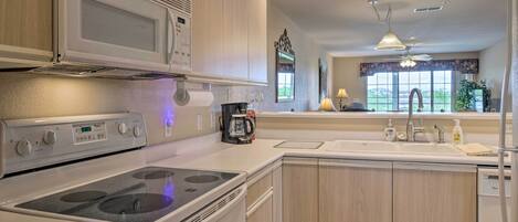 A modern kitchen with a built-in microwave, stove, and oven, wooden cabinets, a sink with a faucet, and a window with a view.