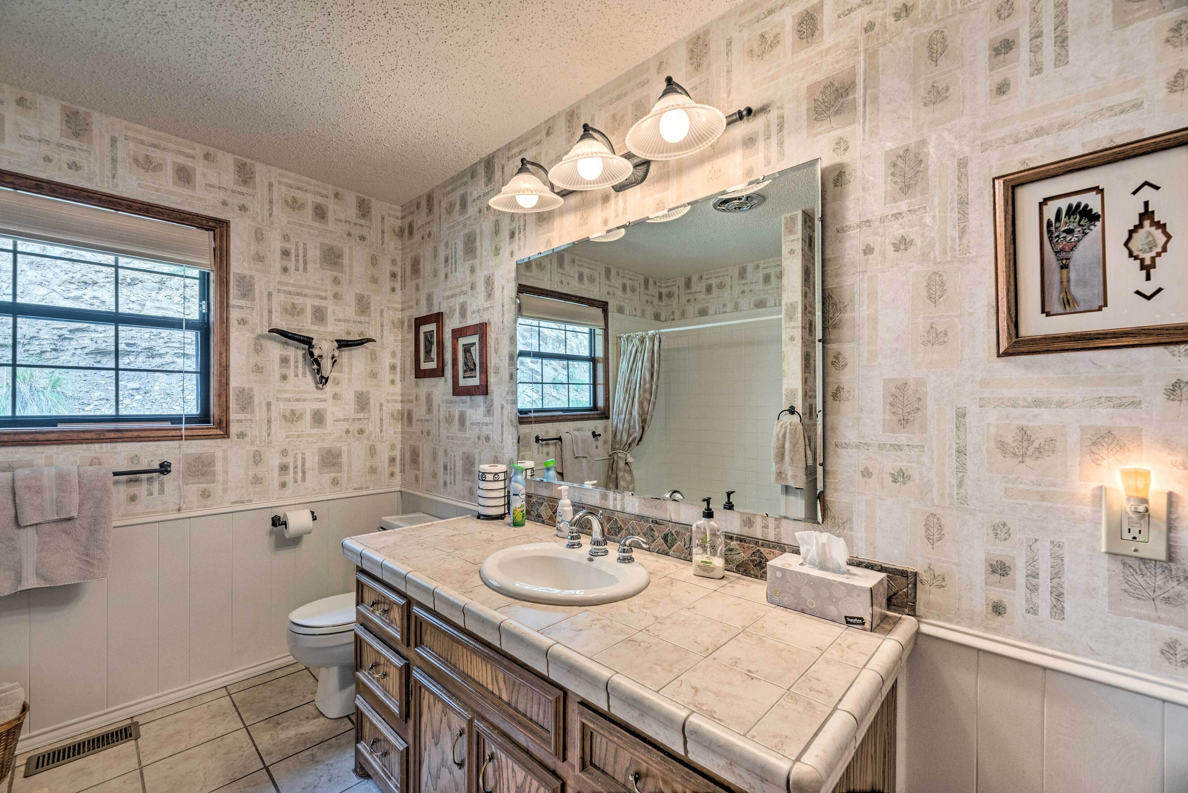 A bathroom with a large mirror, a sink, and a toilet. There are towels hanging on the wall and a window with a view of trees.