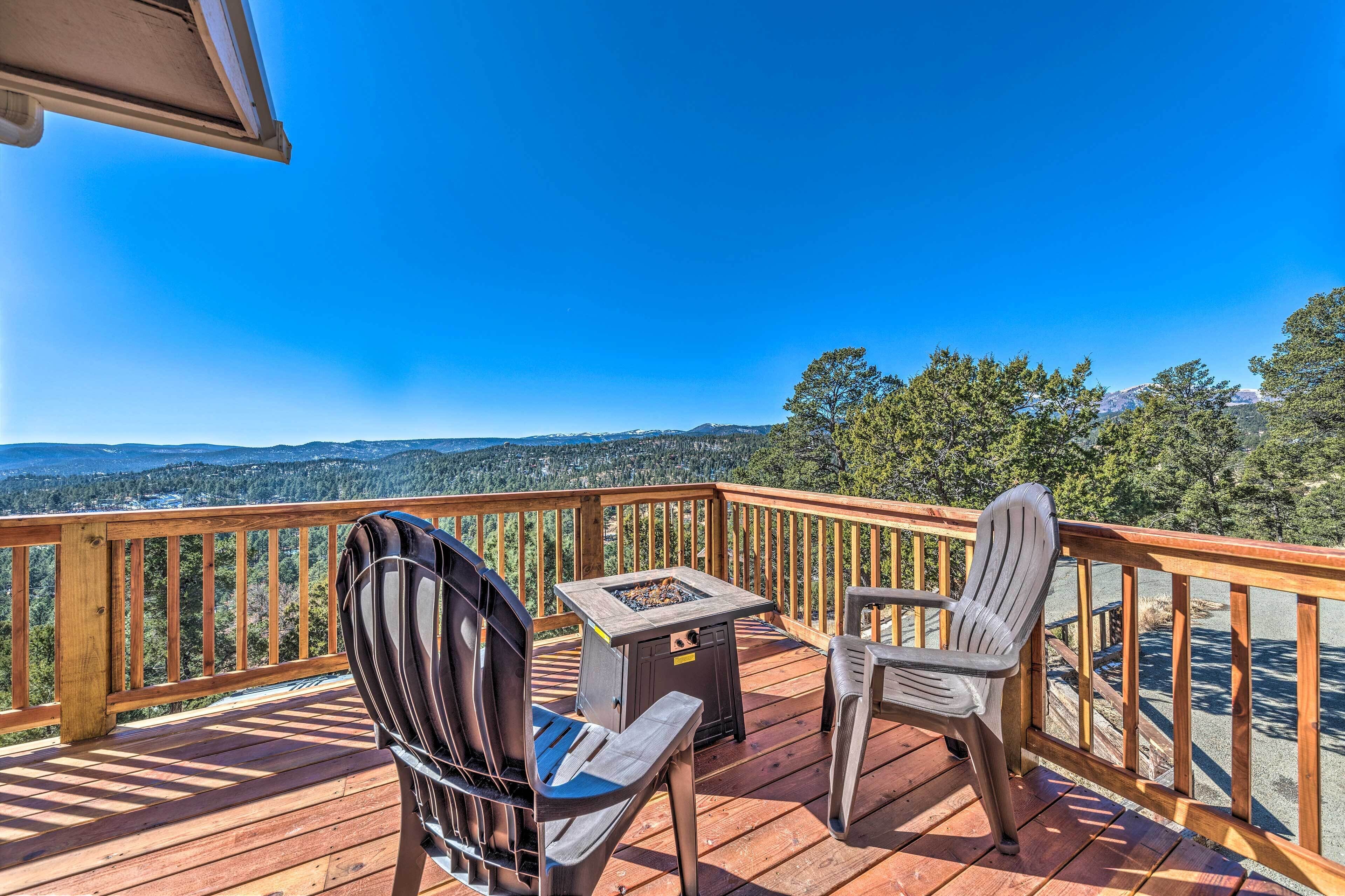 A wooden deck with two Adirondack chairs and a small table, overlooking a mountainous landscape.