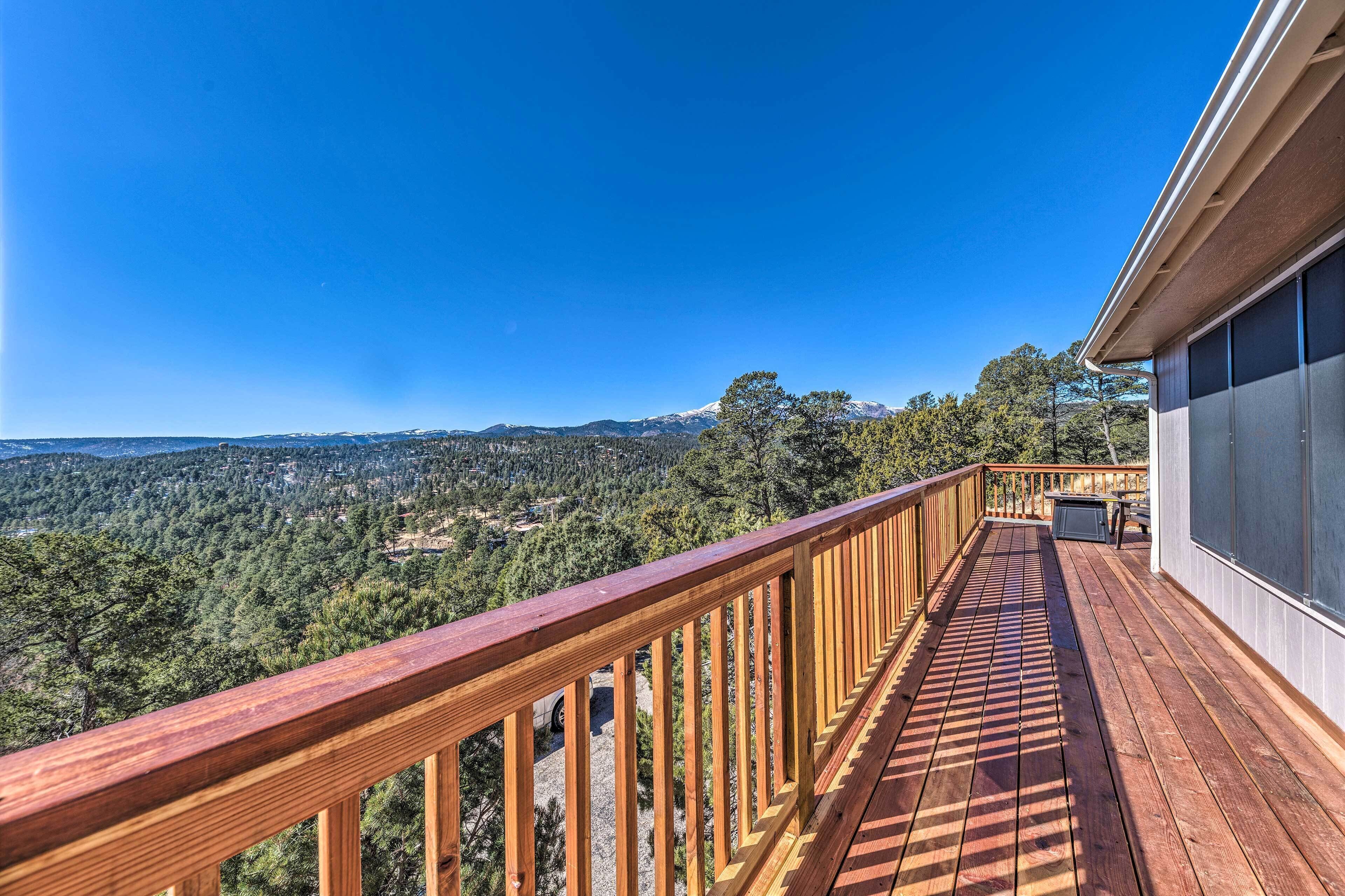 A wooden deck with a view of a forested landscape and mountains.