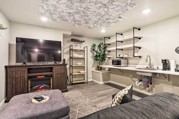 A modern living room with a flat-screen TV, a fireplace, a kitchen area with a sink and countertop, and a dining area with shelves.