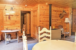 A wooden cabin interior with a dining table, chairs, a fireplace, and a mounted deer head. - Gould City Lakefront Hideaway w/ Dock & Rowboat! (Gould City)