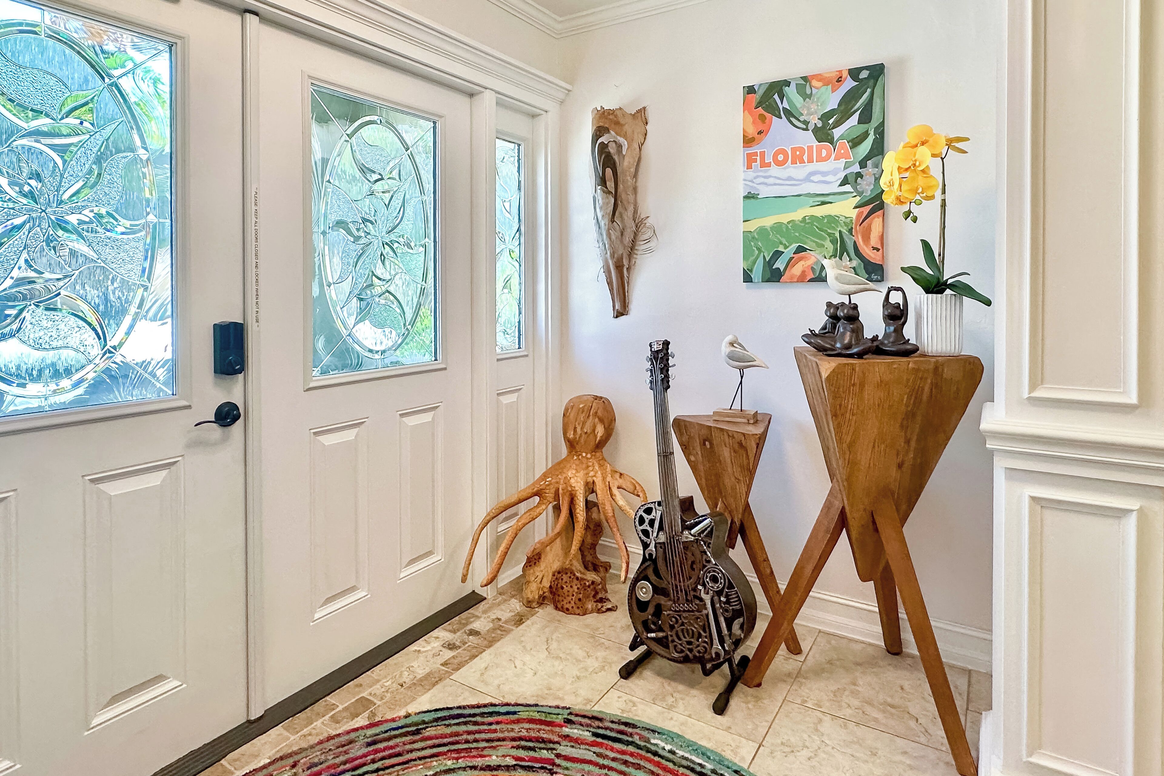 A hallway with a white door, a wooden octopus sculpture, a guitar, and a wooden stand with a vase and a bird figurine.