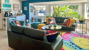 Ein modernes Wohnzimmer mit zwei Sofas, einem Couchtisch und einer Küchenzeile inklusive Kaffeemaschine und Regalen.