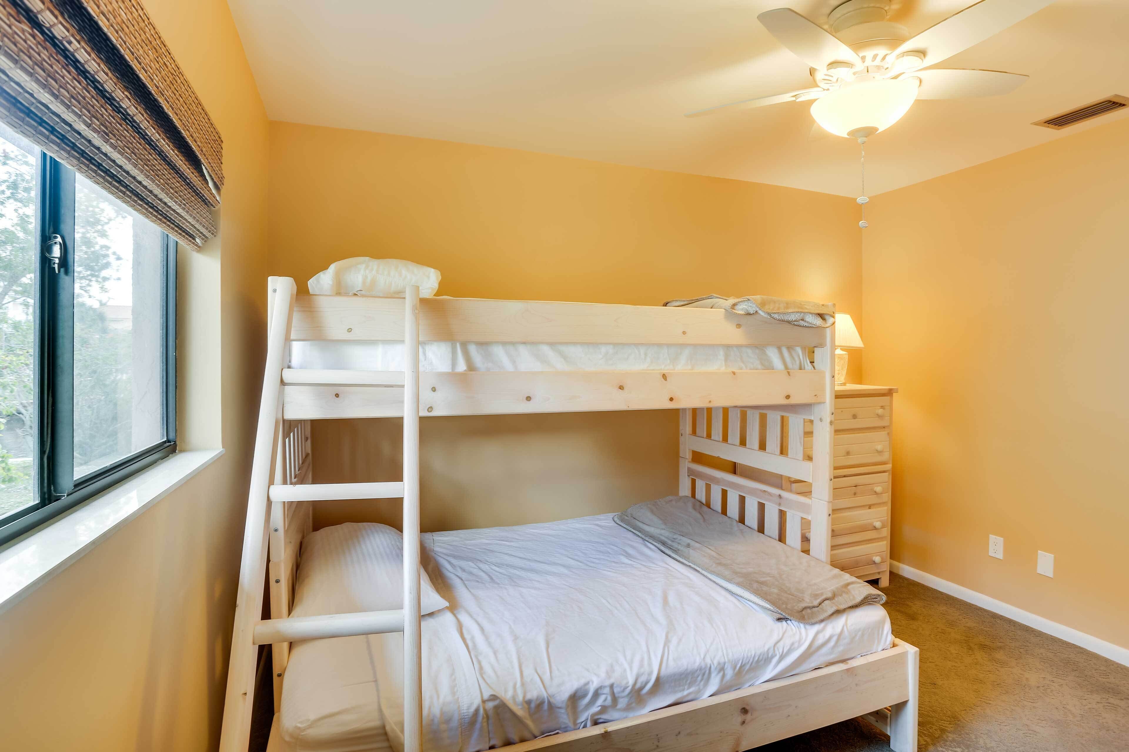 A bunk bed room with a ceiling fan, a window with blinds, and a dresser.