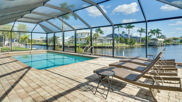 Piscina ao ar livre coberta com espreguiçadeiras e vista para um lago e palmeiras.