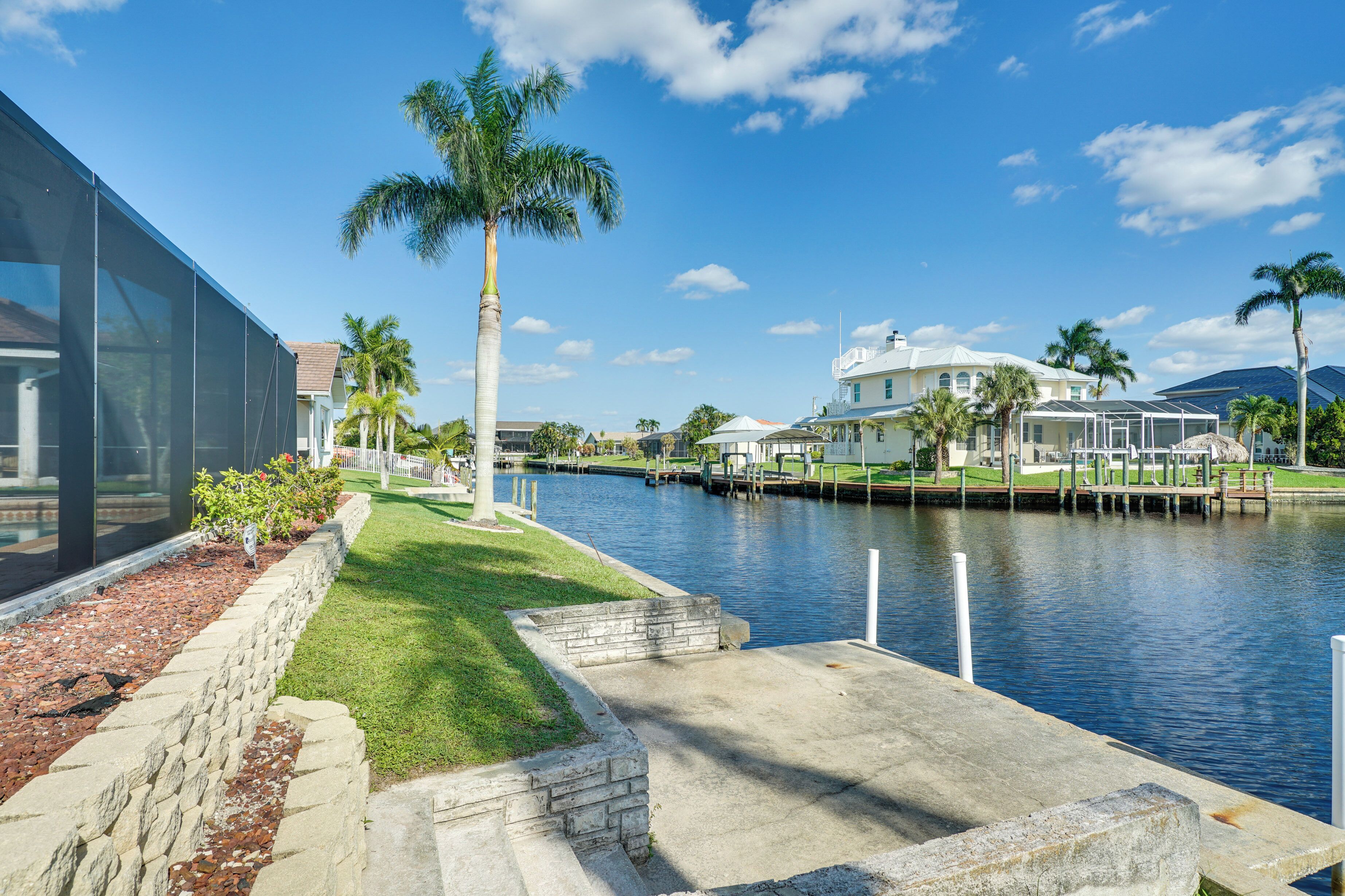 A waterfront property with a dock, palm trees, and a large house with a white roof.