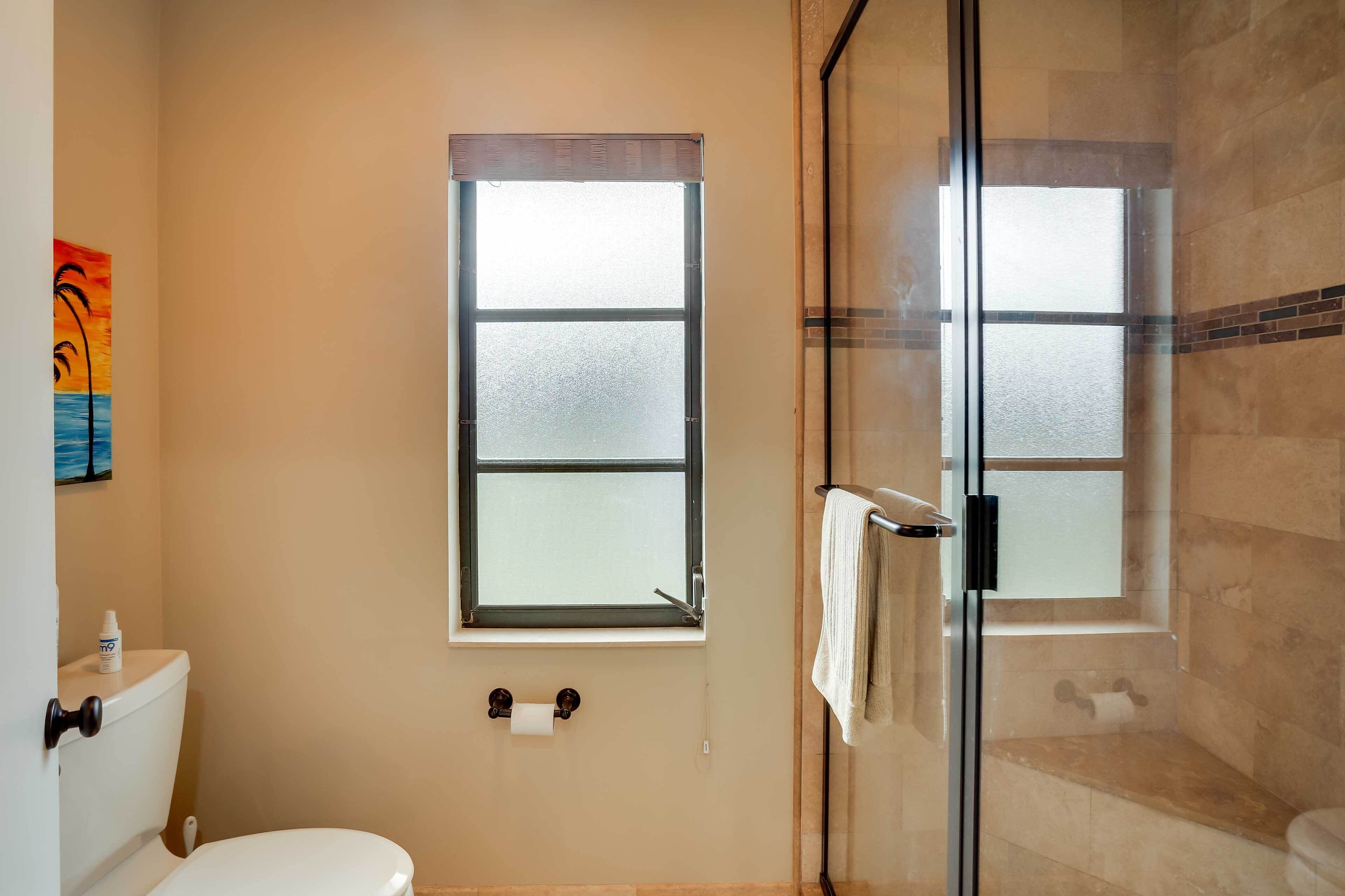 A bathroom with a toilet, a window, and a glass shower enclosure.