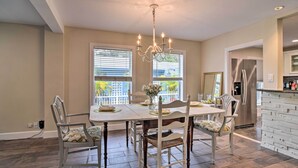 A dining area with a chandelier, white chairs, and a table set for four. - Renovated Ozona Home w/ Views - Steps to Gulf (Palm Harbor)
