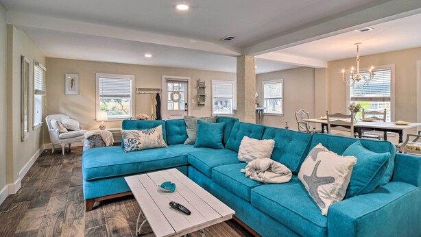 A spacious living room with a teal sectional sofa, a white coffee table, and a dining area with a white table and chairs. - Renovated Ozona Home w/ Views - Steps to Gulf (Palm Harbor)