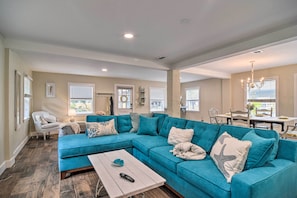 Un salon spacieux avec un canapé d’angle turquoise, une table basse blanche et un coin repas comprenant une table et des chaises blanches.