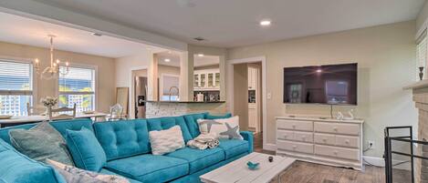 A modern living room with a teal sofa, a white coffee table, and a TV mounted on the wall.