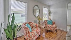 A room with two floral armchairs, a wooden coffee table, a large mirror, and a potted plant. - Bright Carolina Beach Cottage w/ Yard & Grill (Carolina Beach)
