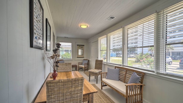 A cozy room with a wooden table, wicker chairs, a sofa with striped pillows, and large windows with blinds. - Bright Carolina Beach Cottage w/ Yard & Grill (Carolina Beach)