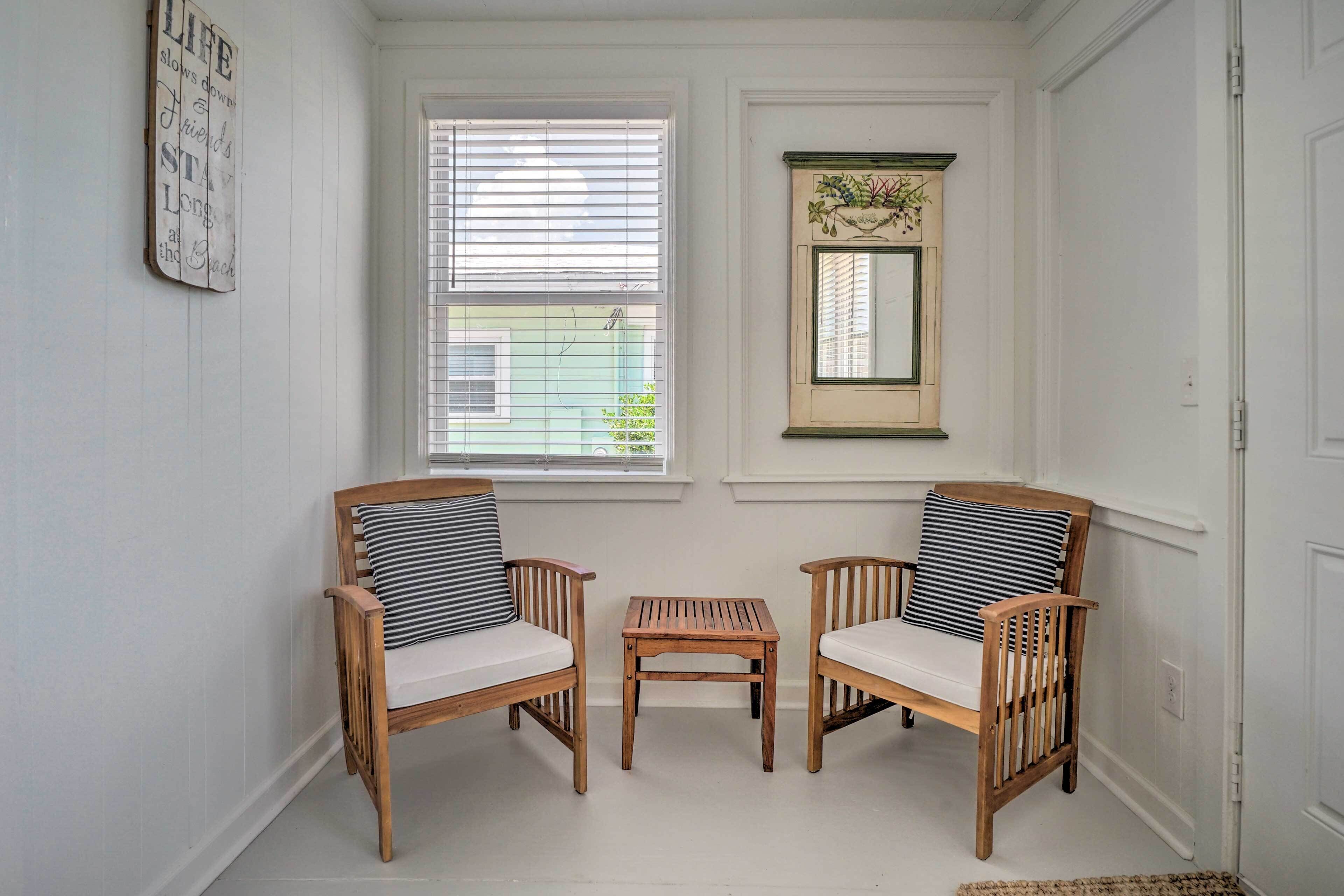A room with two wooden chairs with striped cushions, a small wooden table, and a window with blinds.