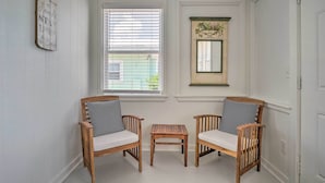 A room with two wooden chairs with striped cushions, a small wooden table, and a window with blinds. - Bright Carolina Beach Cottage w/ Yard & Grill (Carolina Beach)