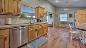 A kitchen with wooden cabinets, a stainless steel dishwasher, a window, and a ceiling fan. - Private Eureka Springs Retreat w/ Hot Tub! (Eureka Springs)