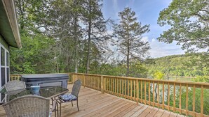 Une terrasse en bois avec une table et des chaises en verre, donnant sur une zone boisée et un plan d’eau.