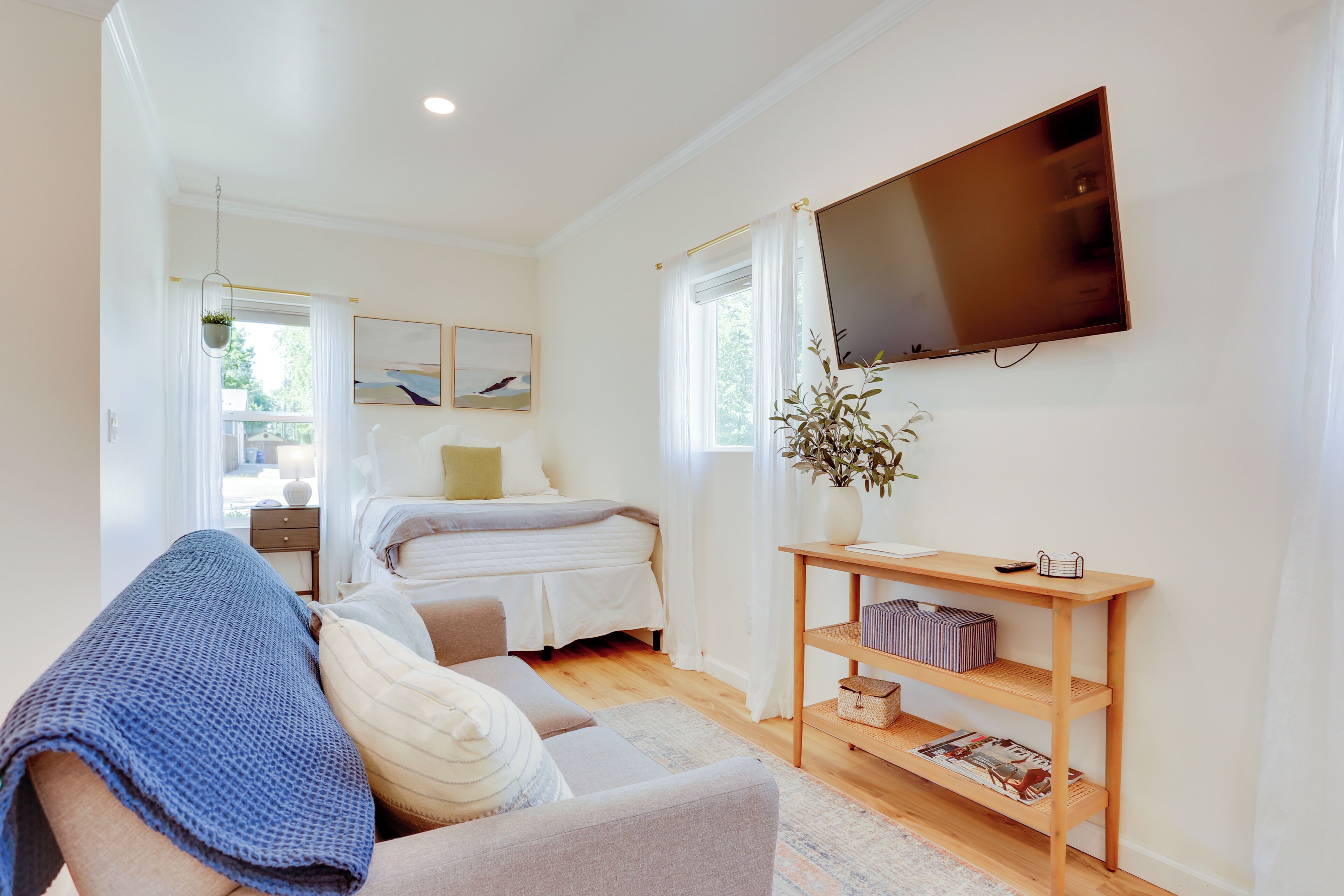 A modern bedroom with a bed, a sofa, a TV, and a wooden shelf with items.