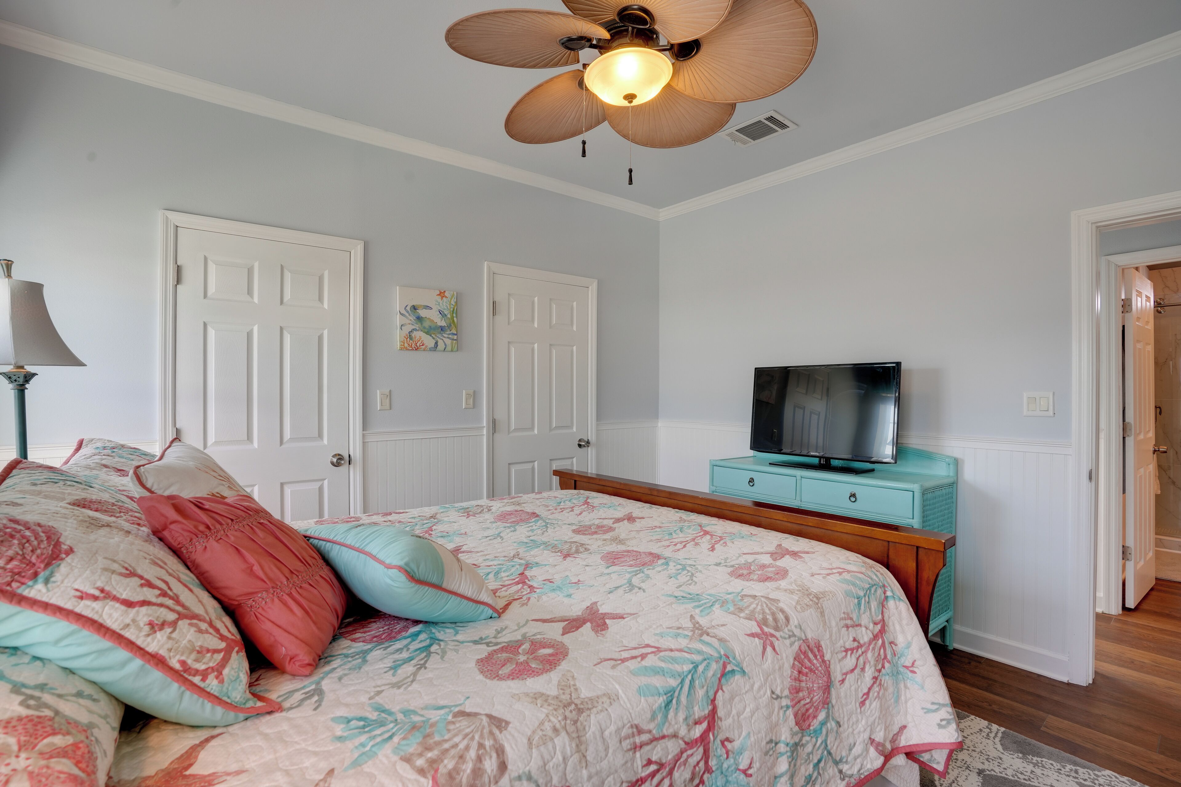 A bedroom with a bed, a ceiling fan, a television on a dresser, and white doors.