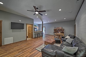 A spacious living area with a wooden floor, a leather sofa, a coffee table, and a ceiling fan.