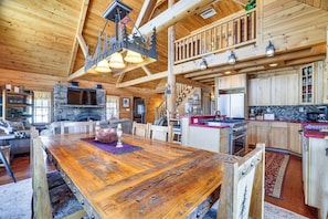 A spacious wooden interior with a large dining table, stone fireplace, and modern kitchen.
