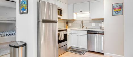A modern kitchen with stainless steel appliances, white cabinetry, and a wooden floor.