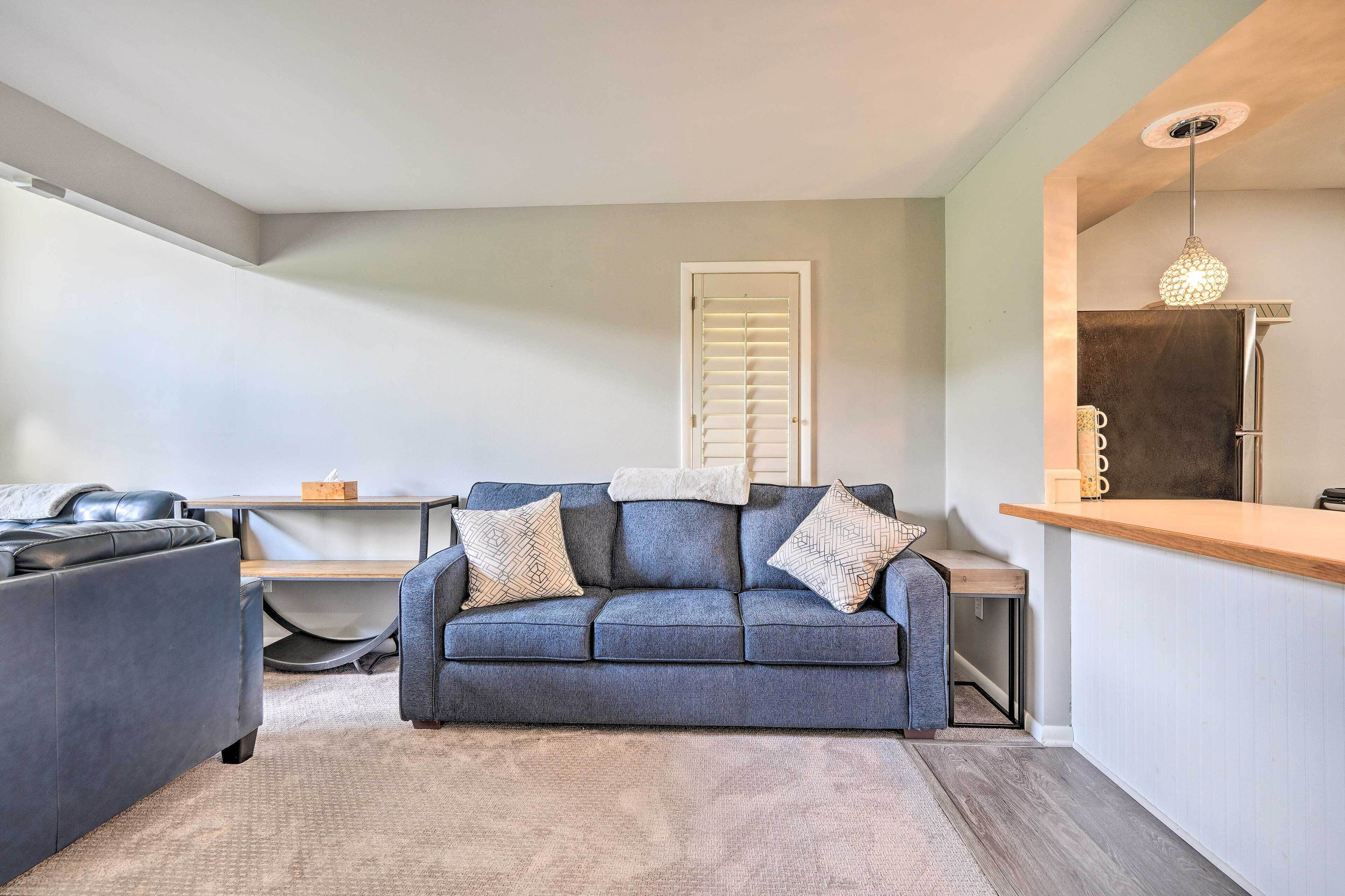 A compact living space with a grey sofa, a small table, and a kitchenette area.