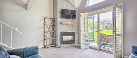 Un salón amplio con chimenea de piedra, ventilador de techo y un gran ventanal corredero que da a un patio.