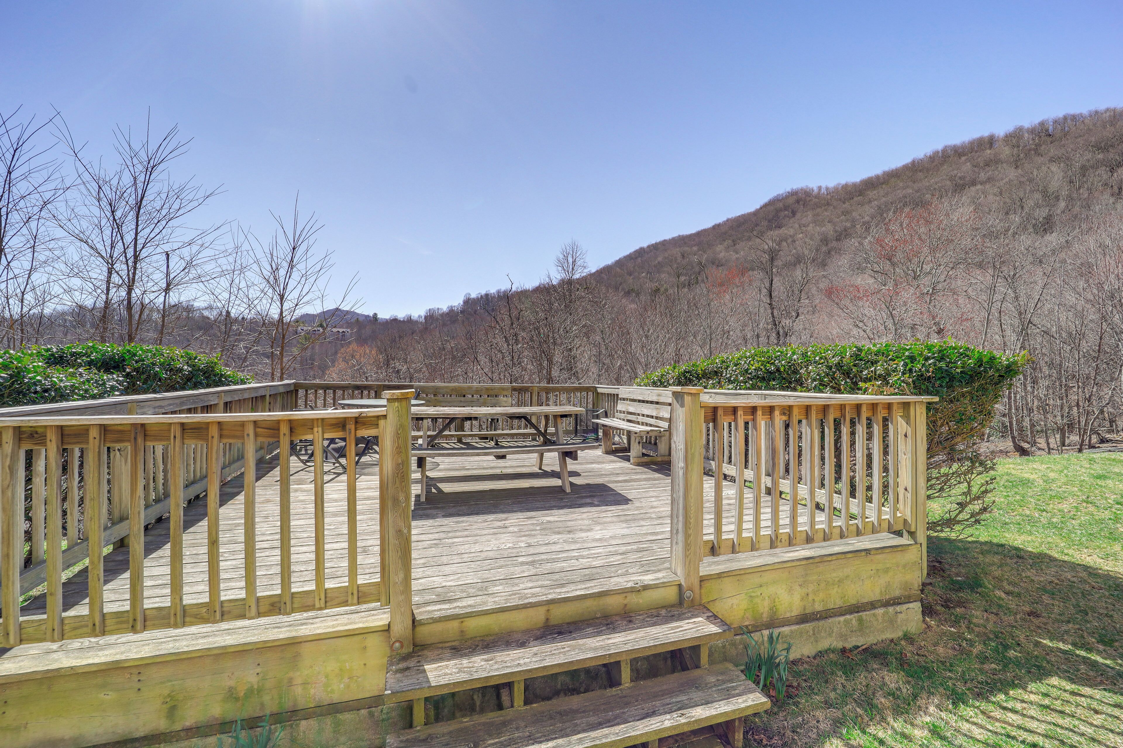 A wooden deck with picnic tables and benches, surrounded by trees and a grassy area.