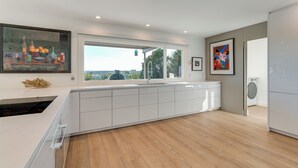 A modern kitchen with a large window, white cabinetry, and a view of the outdoors. - Luxe Mid-century Austin Home w/ Canyon Views (Austin)