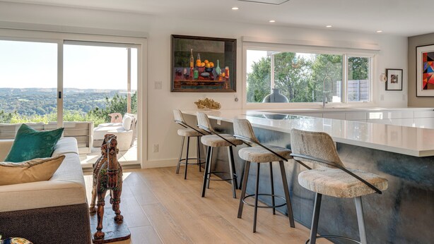A modern kitchen with a bar area, large windows, and a view of the landscape. - Luxe Mid-century Austin Home w/ Canyon Views (Austin)