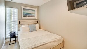 Une chambre à coucher comprenant un lit, une table de chevet, une fenêtre avec des stores, un tableau accroché au mur et un téléviseur fixé au mur.