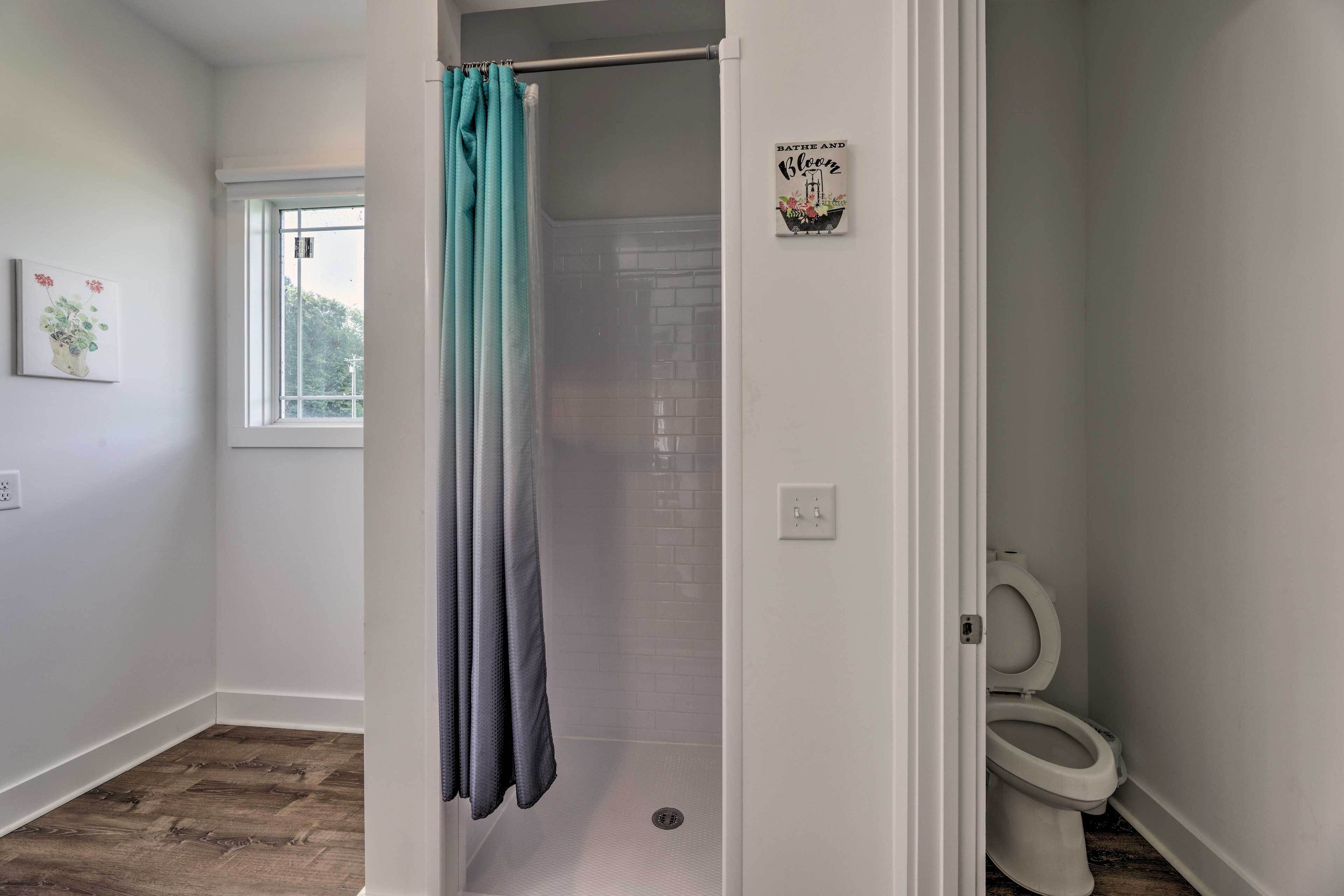 A bathroom with a shower, a toilet, and a window.