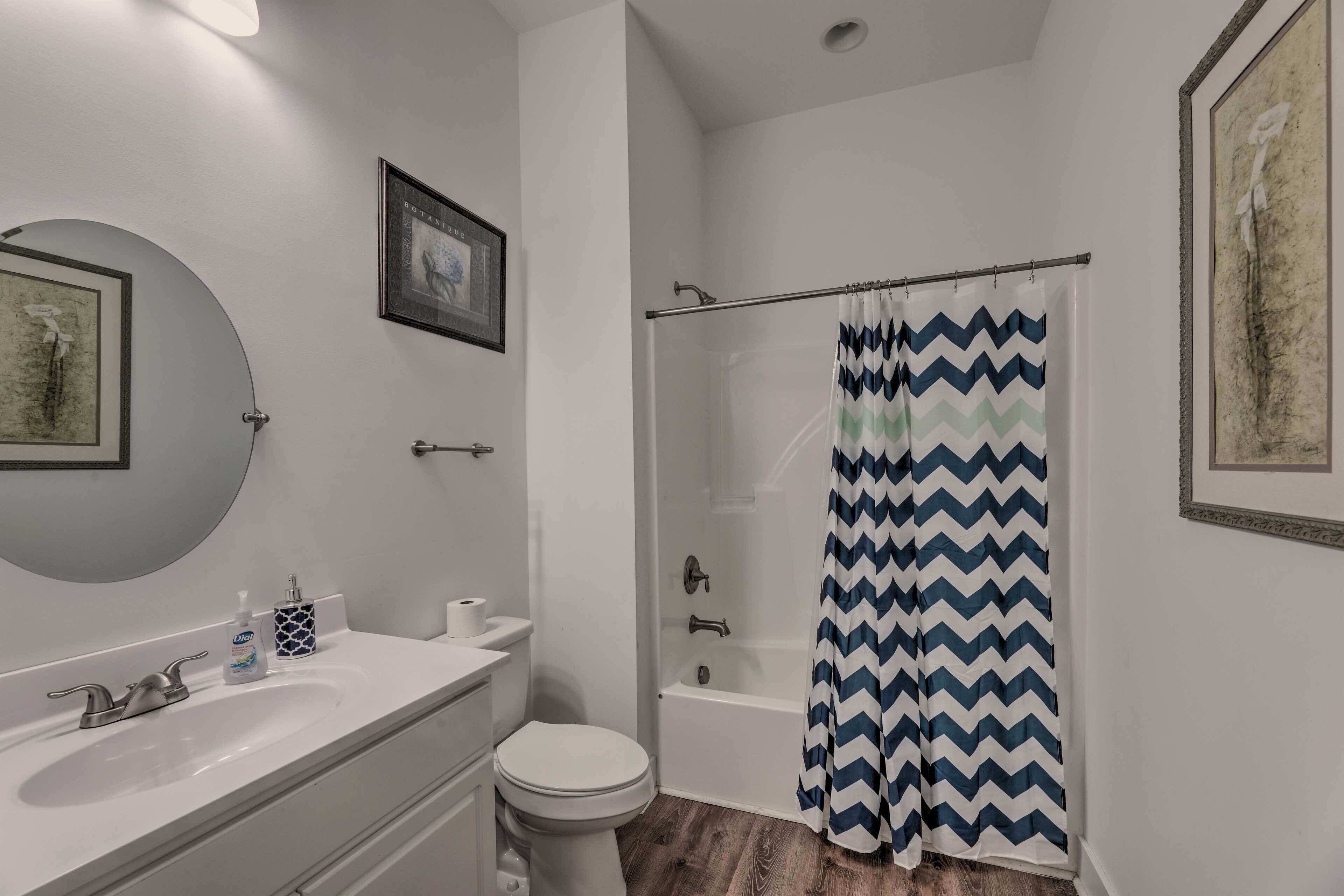 Et badeværelse med en hvid vask, toilet og badekar. Væggene er udsmykket med billeder, og bruseforhænget har et zigzag-mønster.