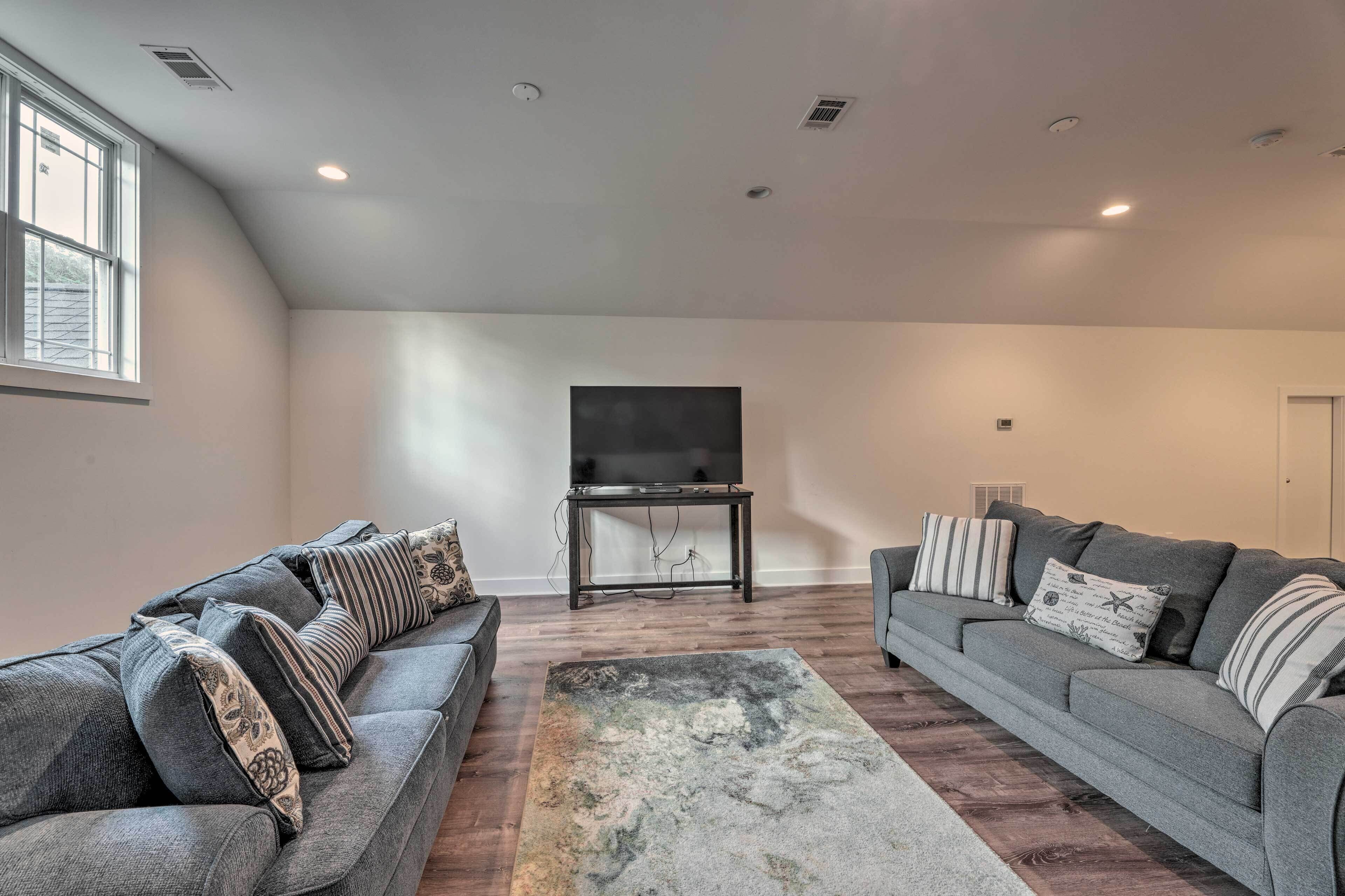 A living room with two grey sofas, a flat-screen TV on a stand, and a patterned rug.