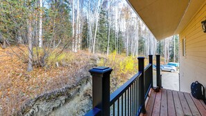 A wooden deck with a black railing, overlooking a forested area with autumn foliage. - Convenient Fairbanks Guest Suite w/ Grill! (Fairbanks)