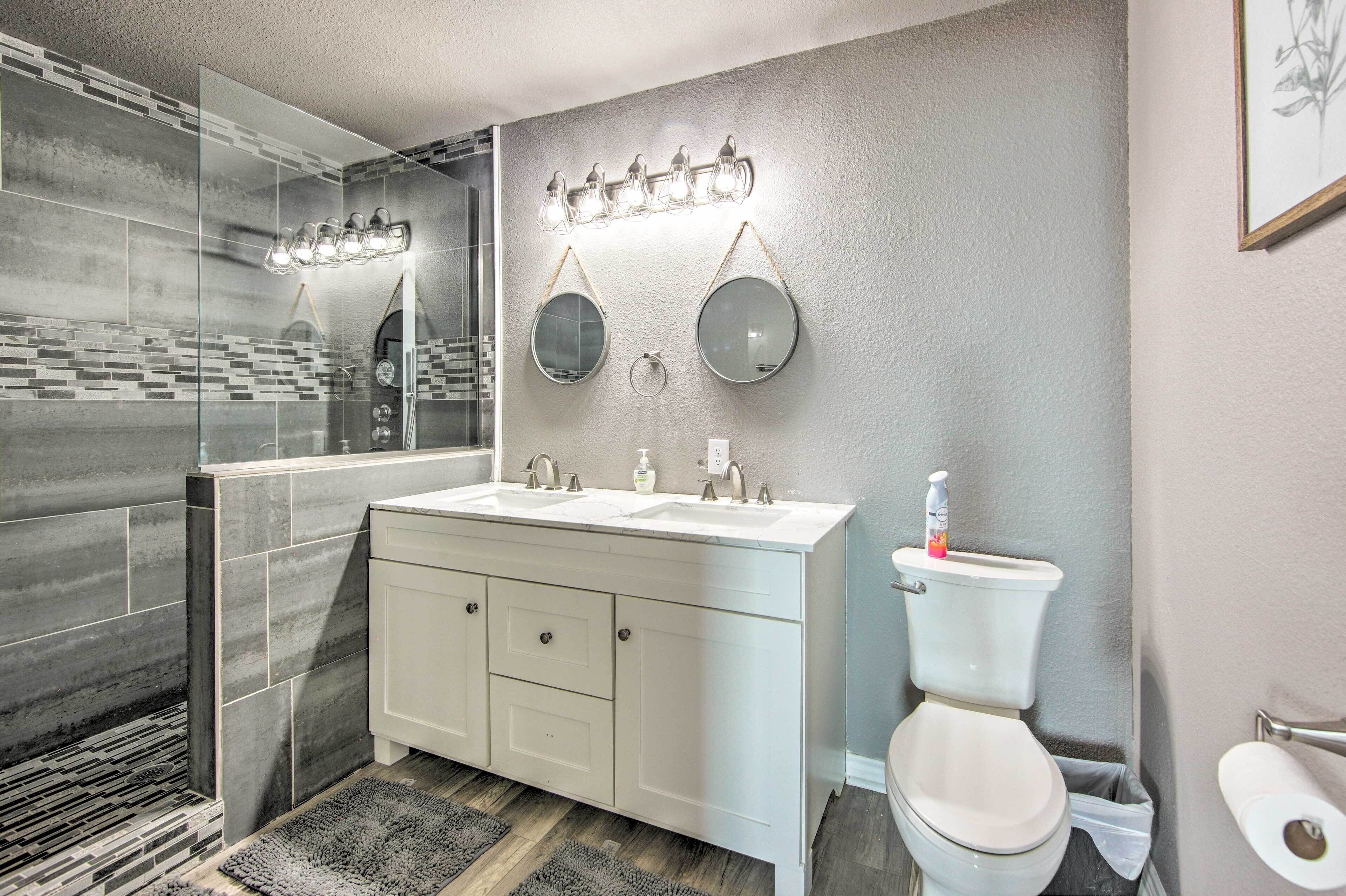 A modern bathroom with a glass shower enclosure, a white vanity with two sinks, a toilet, and a wall-mounted light fixture.