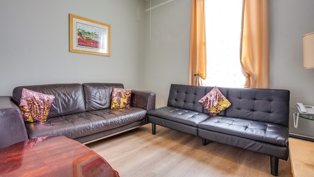 A living room with two leather sofas, a wooden coffee table, a framed picture on the wall, and a window with curtains.