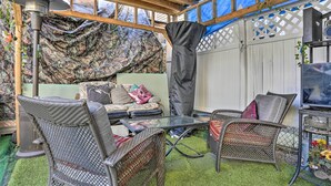 An outdoor patio with wicker furniture, a glass table, and a TV on a metal stand.