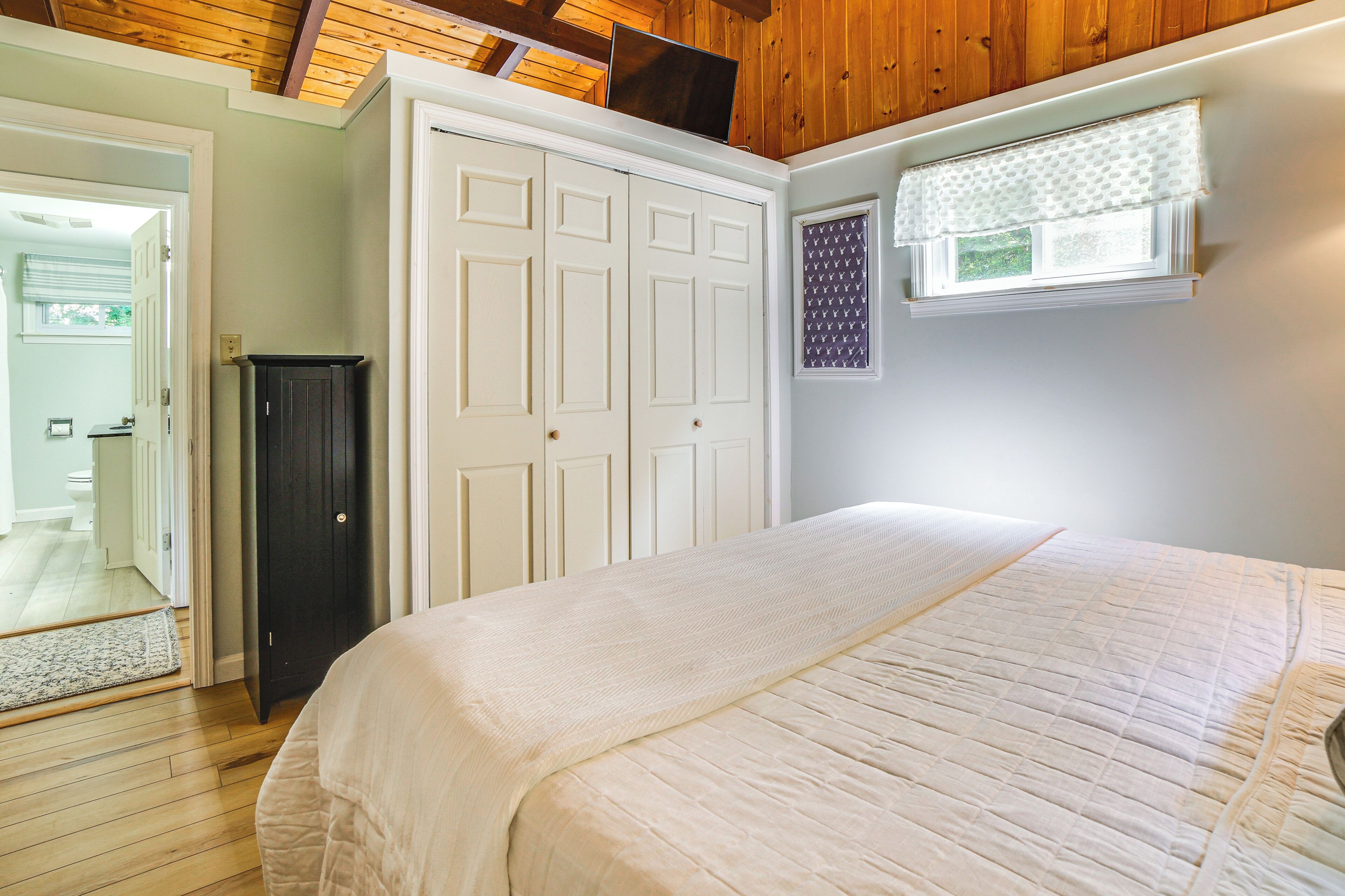 Une chambre à coucher comprenant un lit, une armoire, une fenêtre avec des stores et une porte donnant sur une autre pièce.