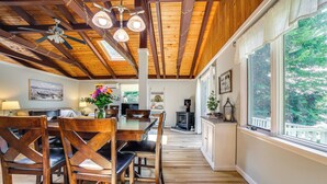 A dining area with wooden chairs and a table, a ceiling fan, and a view of the outdoors through large windows. - Breathtaking Newbury Cottage w/ Deck on Chalk Pond (Newbury)