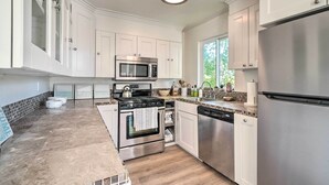 A modern kitchen with white cabinets, stainless steel appliances, a tiled backsplash, and a window providing natural light.