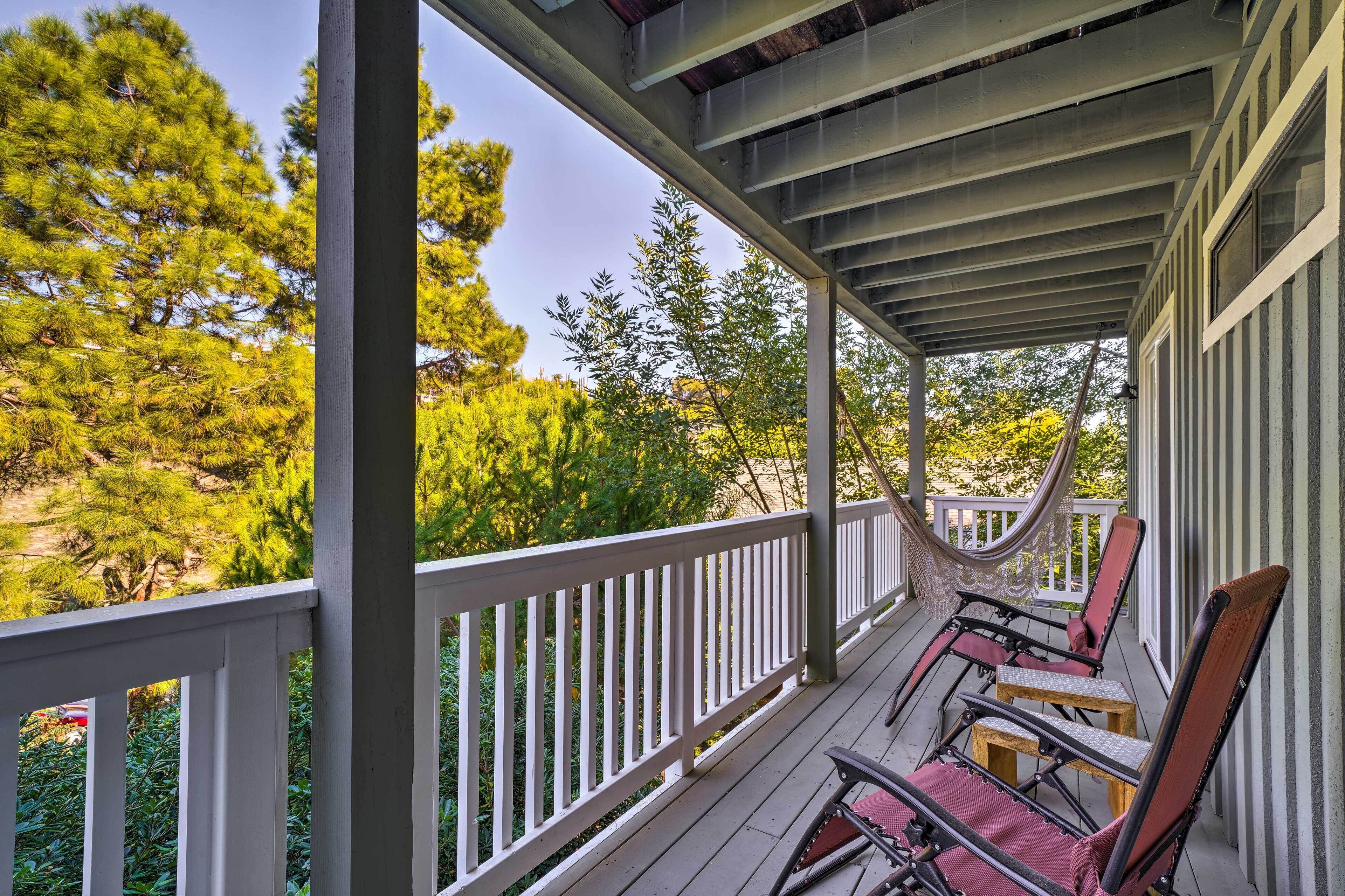 A covered porch with a white railing, wooden chairs, and a hammock.