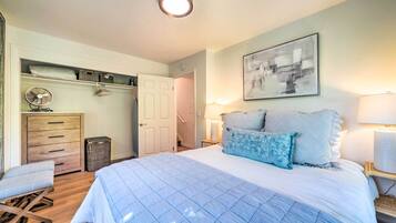A bedroom with a bed, bedside lamps, a ceiling fan, a dresser, and a door leading to another room.