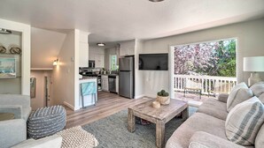 A spacious living area with a sofa, coffee table, and ottoman, a kitchen with modern appliances, and a balcony with a view of trees.