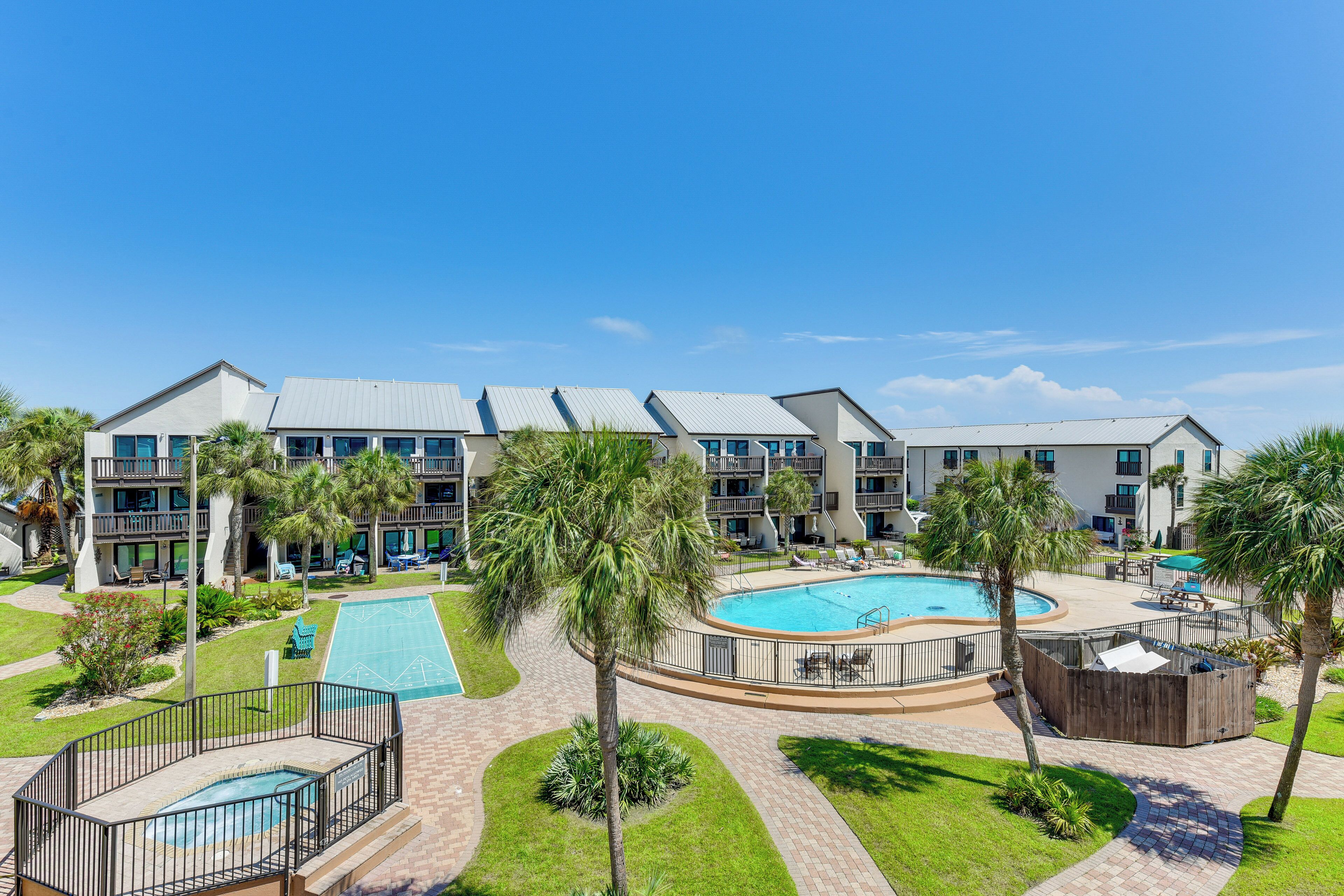 A hotel with multiple balconies, a central swimming pool, and surrounding palm trees.