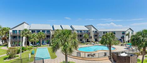 A hotel with multiple balconies, a central swimming pool, and surrounding palm trees.