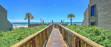 A wooden boardwalk leading to a beach with palm trees and umbrellas.