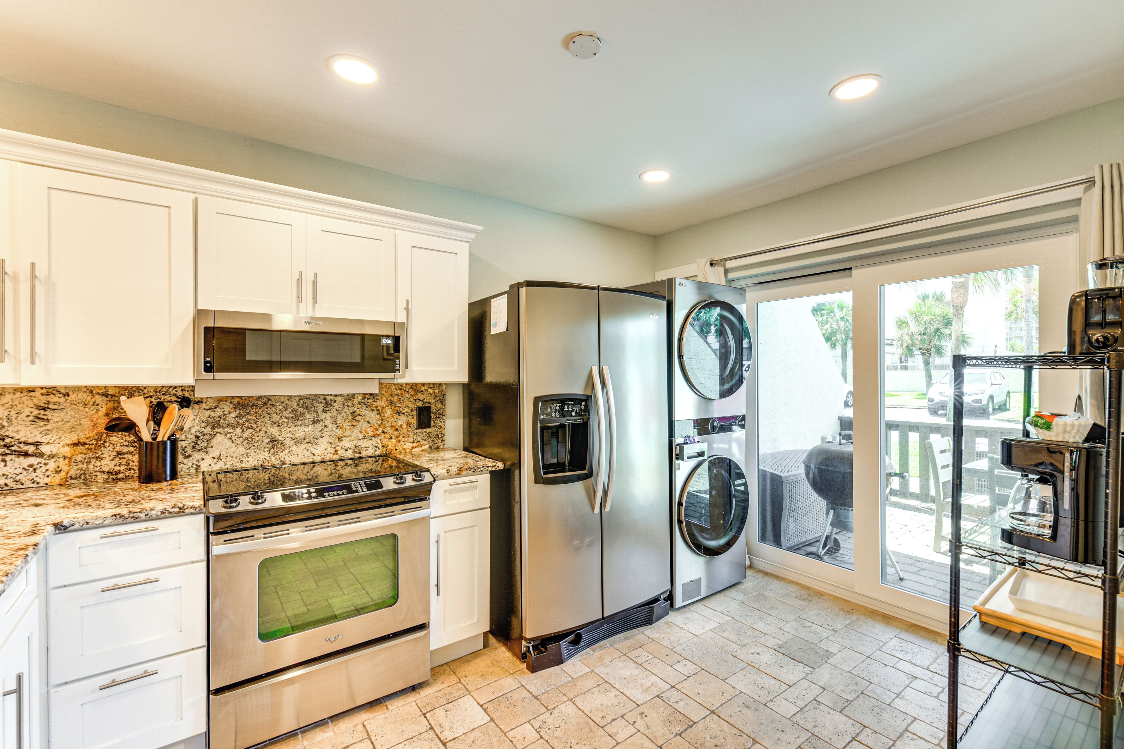 A kitchen with white cabinets, stainless steel appliances, a granite countertop, and a view of the outdoors.